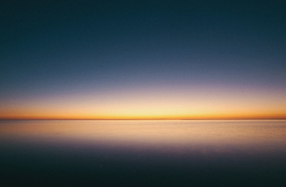 Calm sea horizon at dusk, deep navy sky fading to a thin line of gold