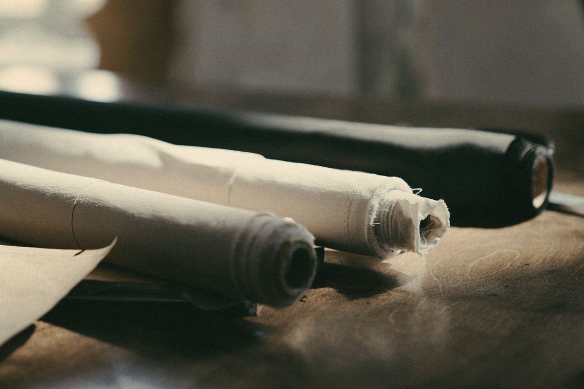 Rolls of cream, white and black fabric on a wooden workshop table in soft window light