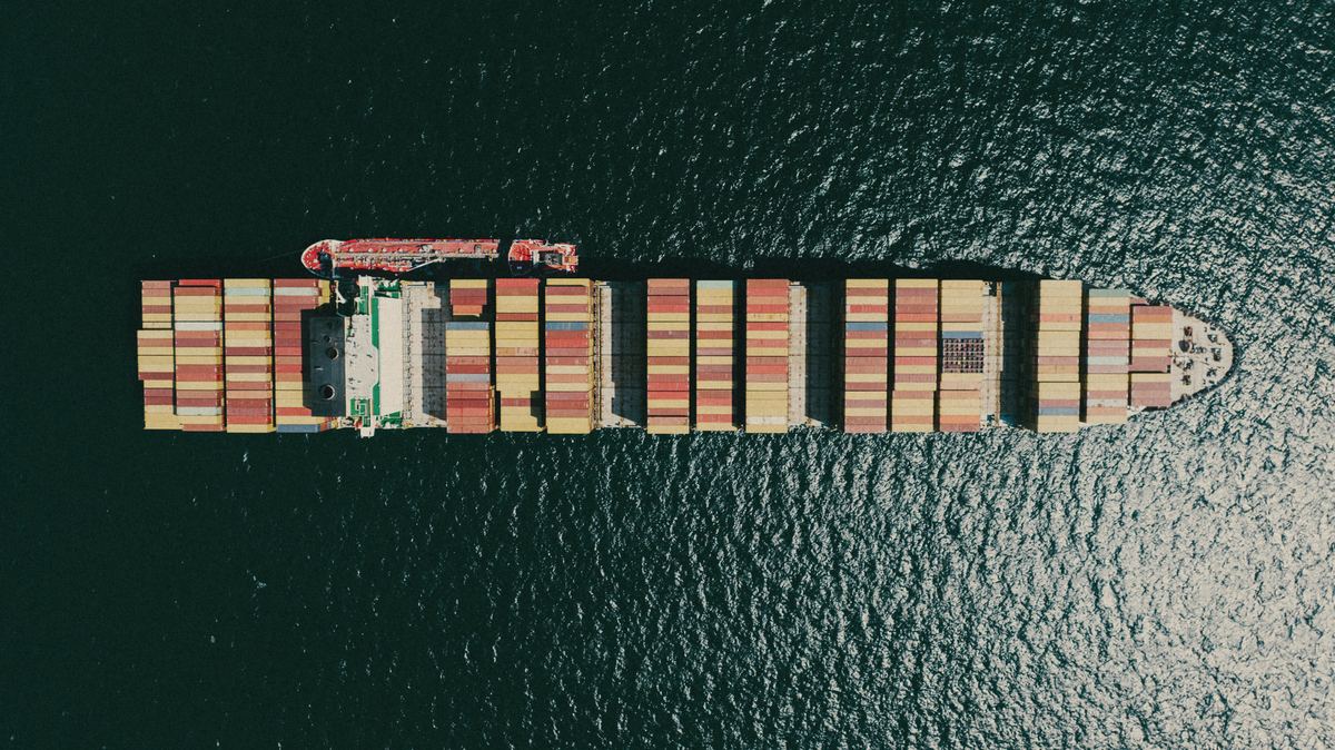 Aerial view of a container ship loaded with ochre and rust containers crossing dark, glinting sea